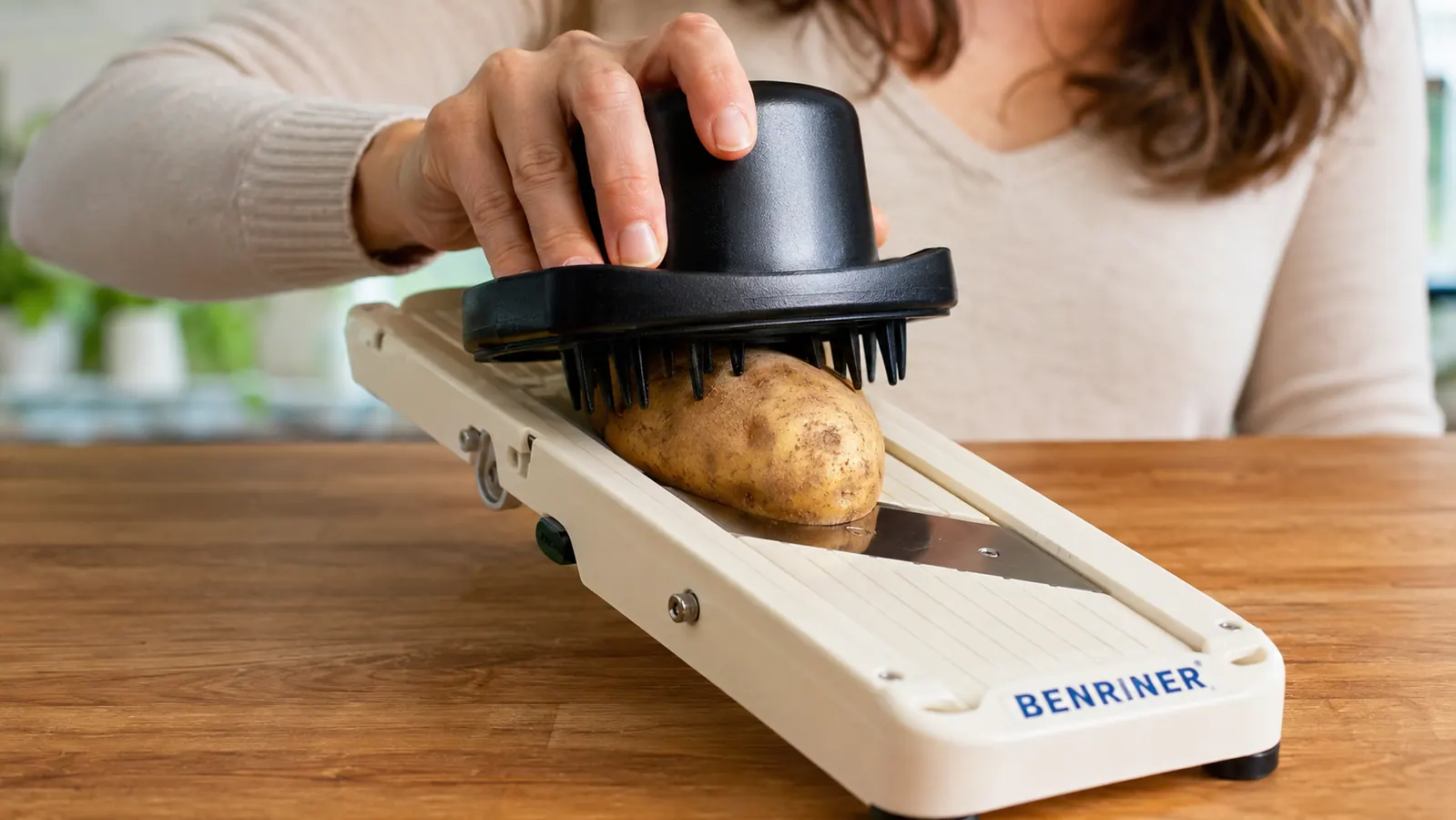 Hand using the safety guard to push a potato across the Benriner mandoline blade