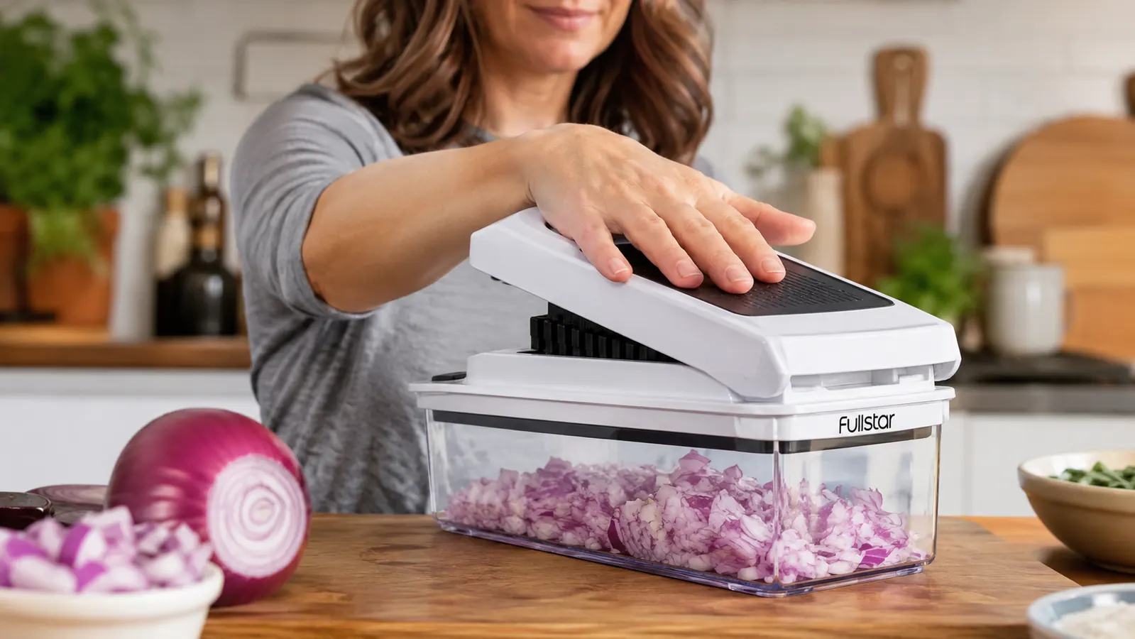 A hand pressing the Fullstar Vegetable Chopper handle to dice an onion into the container