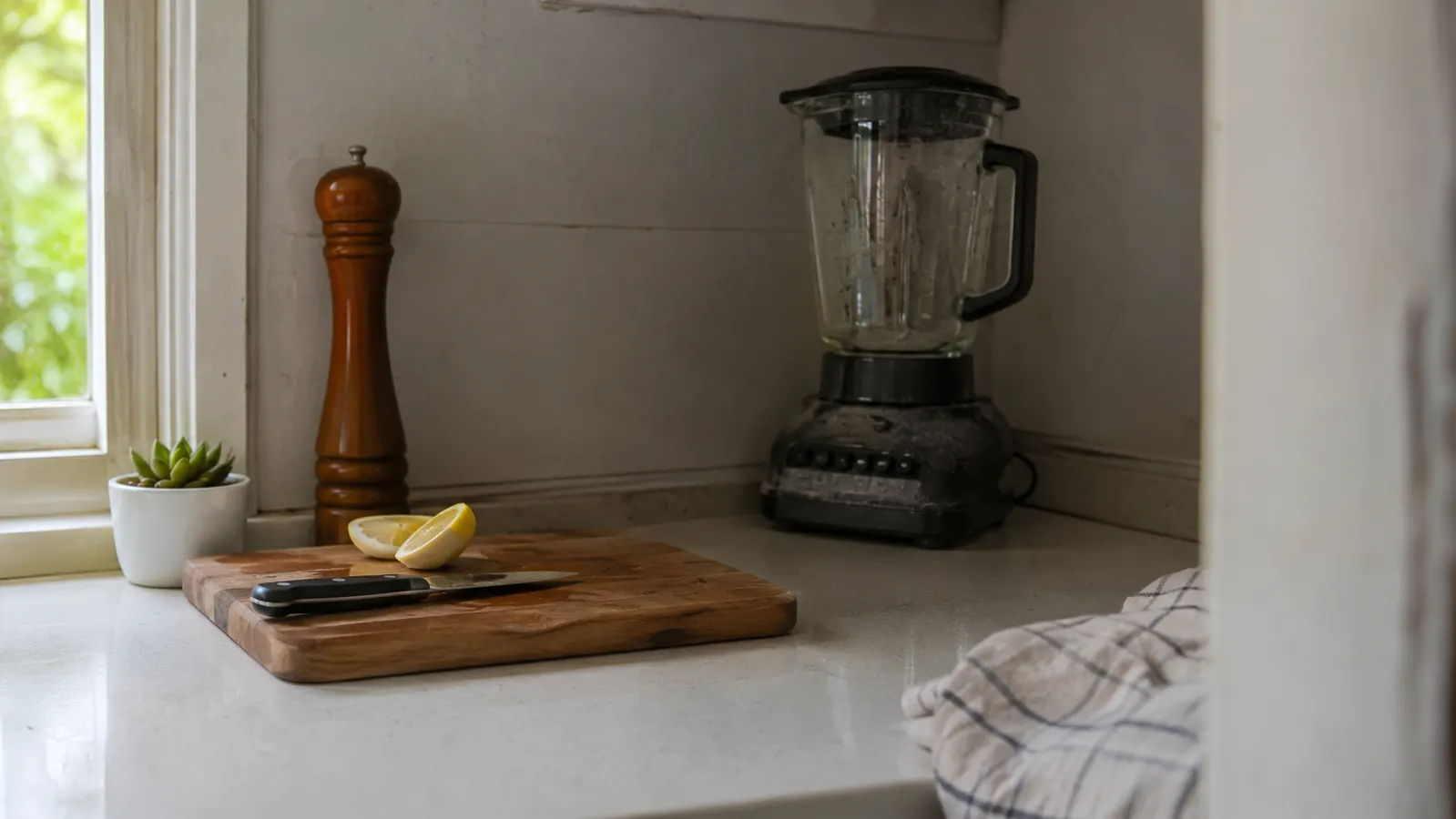 Countertop blender pitcher sitting unused and pushed to the back corner of a kitchen counter