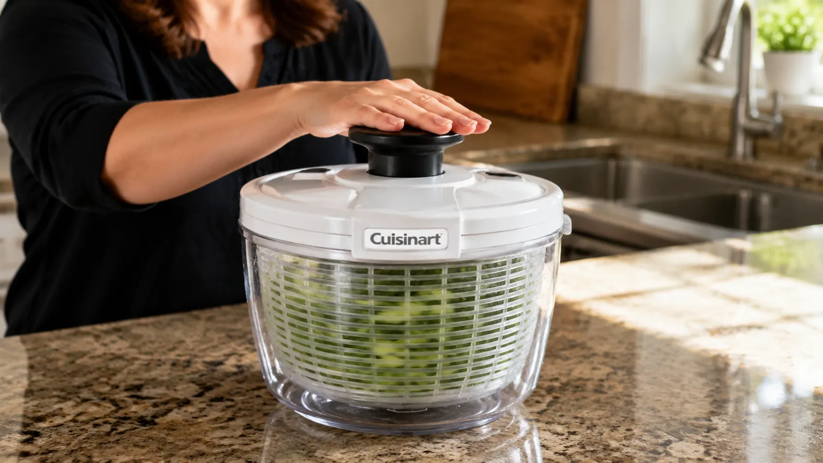 Hands pumping the top of a Cuisinart salad spinner filled with wet lettuce leaves over a kitchen sink